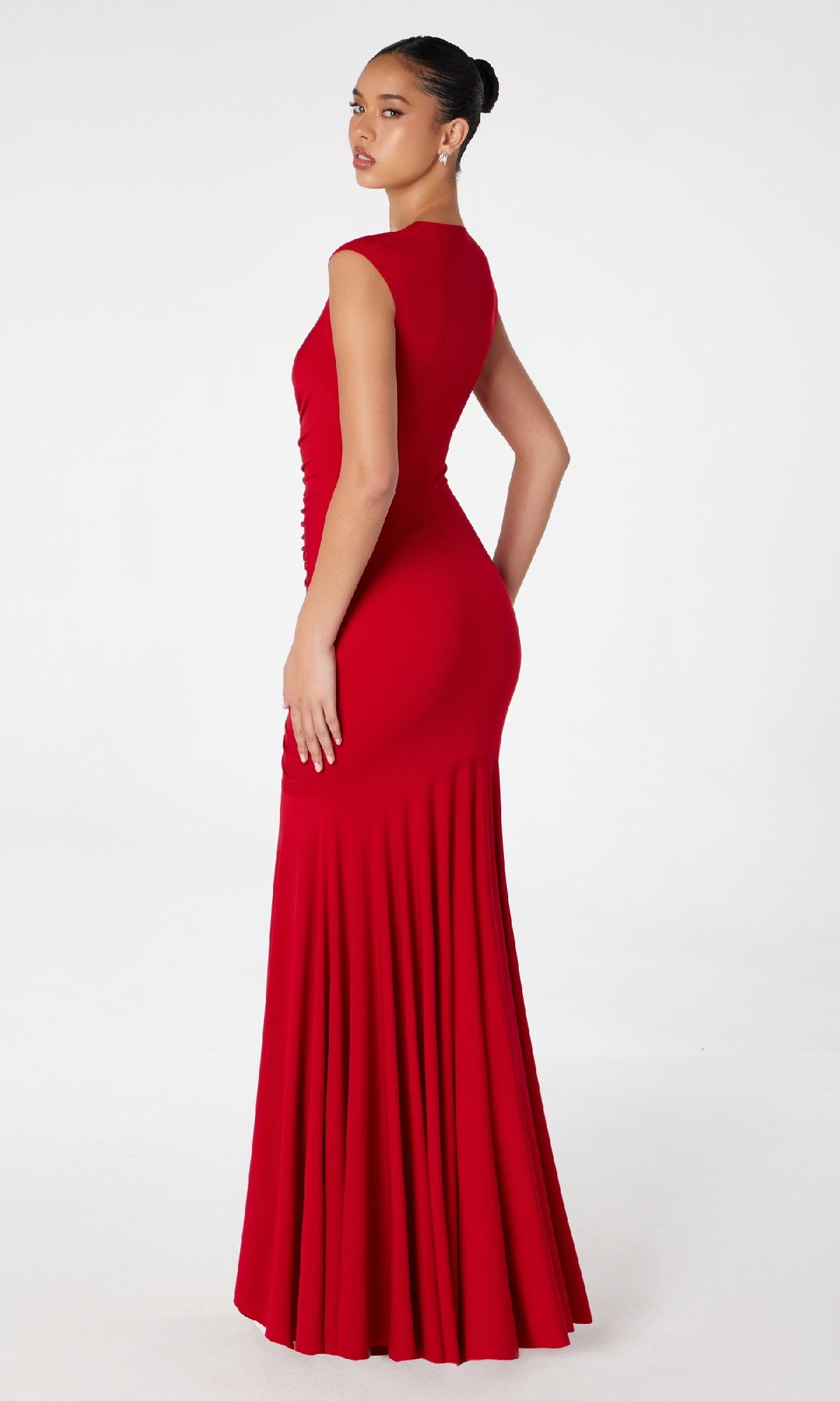 A woman poses in a studio with a white background, showcasing the Cap-Sleeve Long Ruched Prom Dress: Astee T2009, her back slightly turned to highlight the dress’s elegant design.
